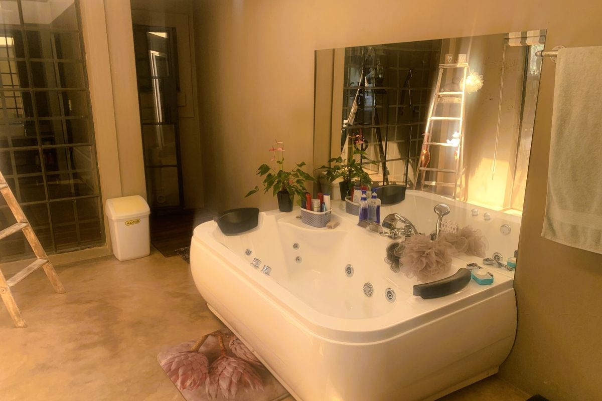 A spacious bathroom featuring a large built-in jetted bathtub, a wall-mounted mirror, and polished concrete flooring.