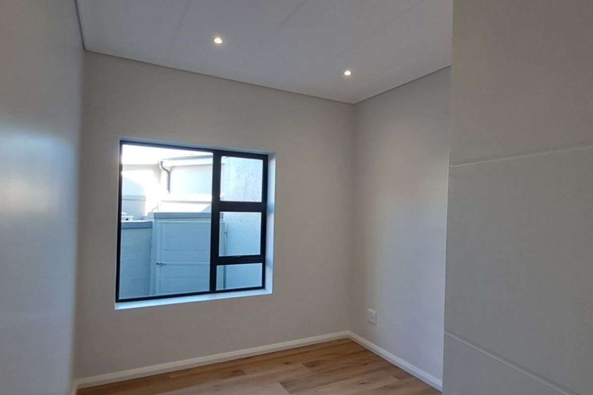 A bright, empty bedroom featuring modern laminate flooring, neutral walls, and recessed ceiling lighting.