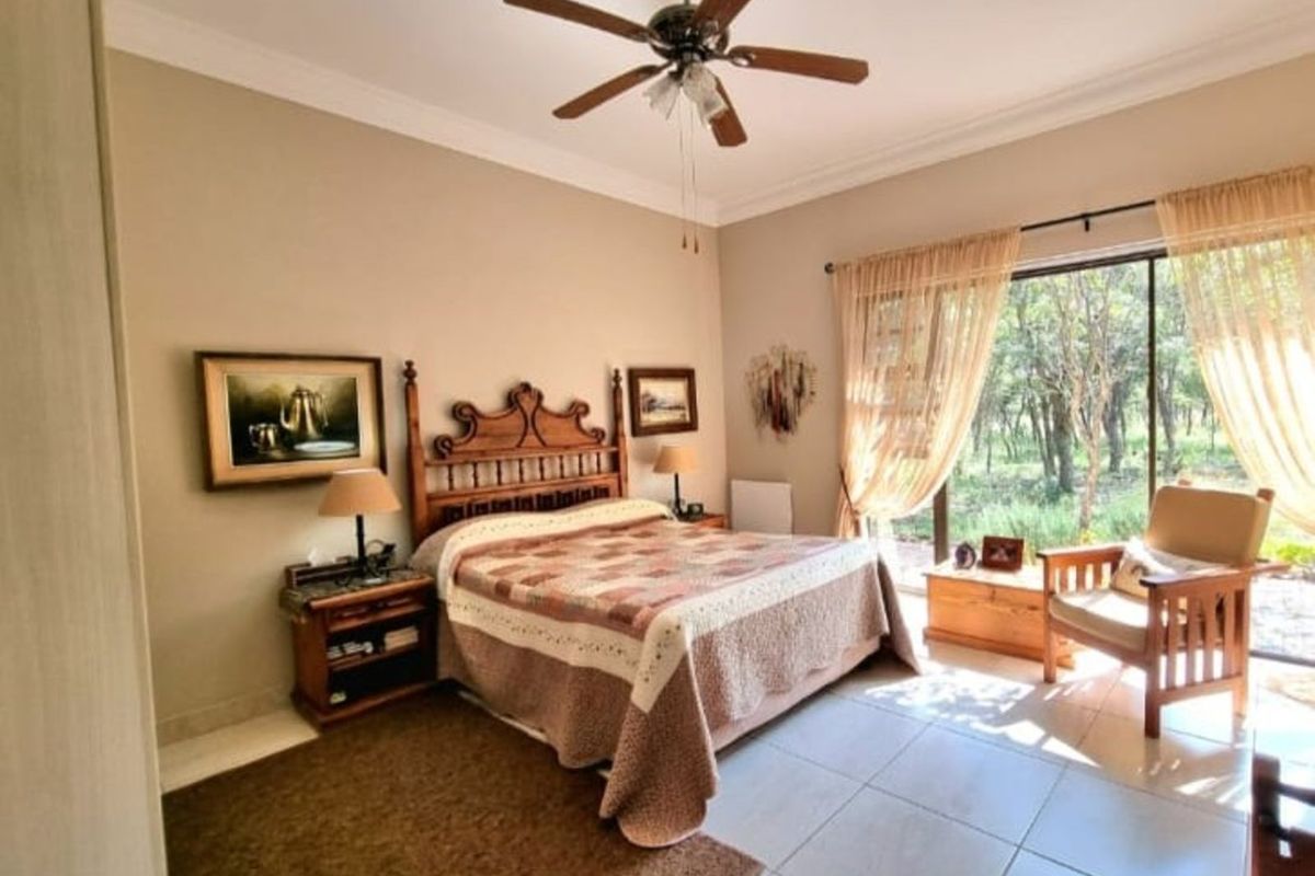 A spacious bedroom featuring large sliding glass doors that provide natural light and views of the surrounding greenery, complemented by a ceiling fan.
