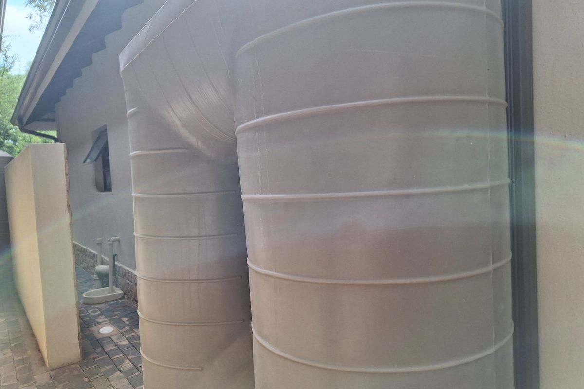A view of the side exterior of the property featuring a large integrated water storage tank and paved walkway.