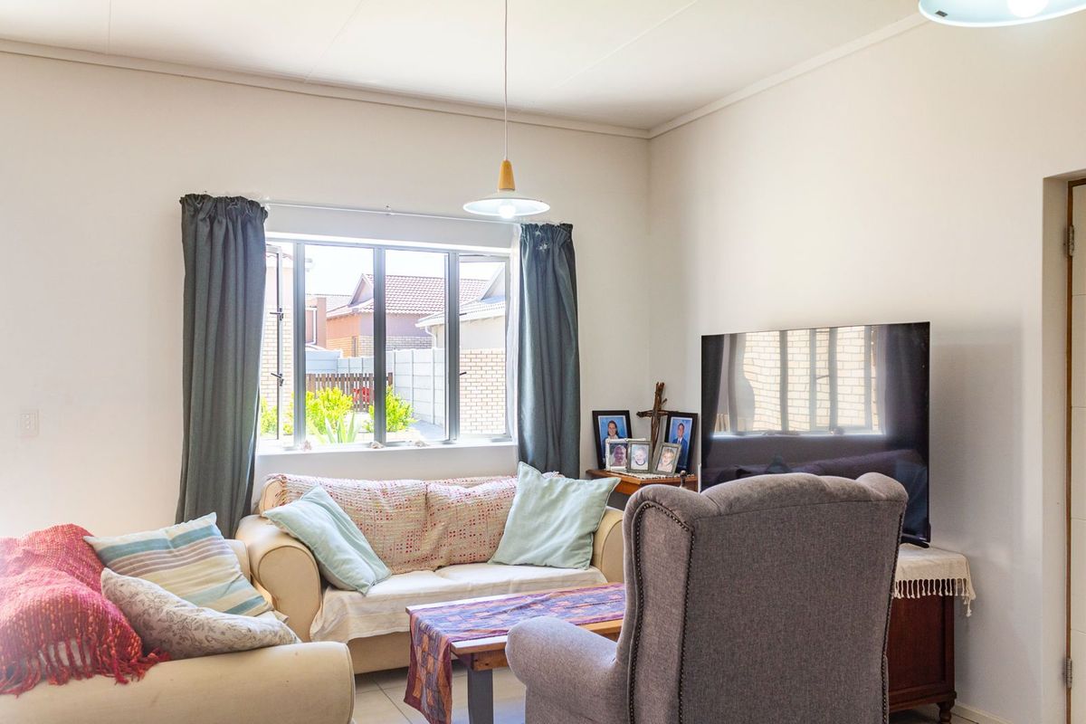 A comfortable living room featuring tiled flooring, a large window providing natural light, and a central pendant light fixture.