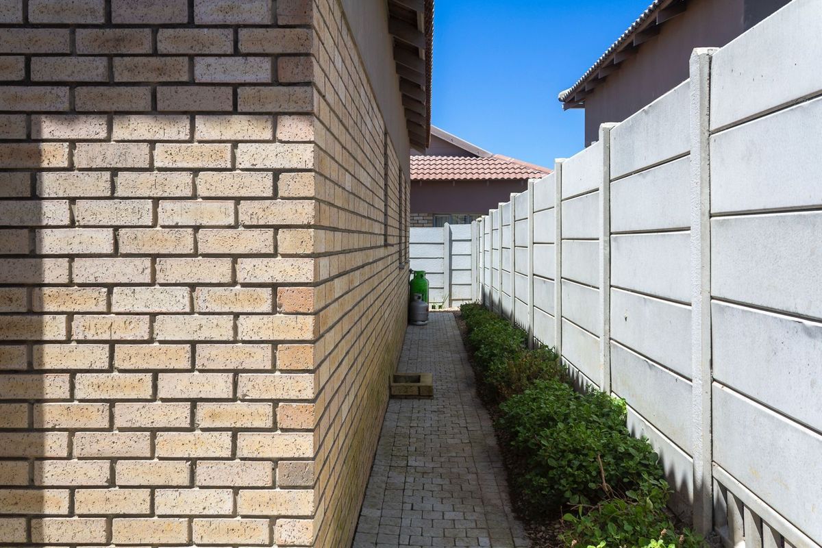 A side passage of the house featuring paved walkway, brick exterior wall, and precast concrete boundary walling.