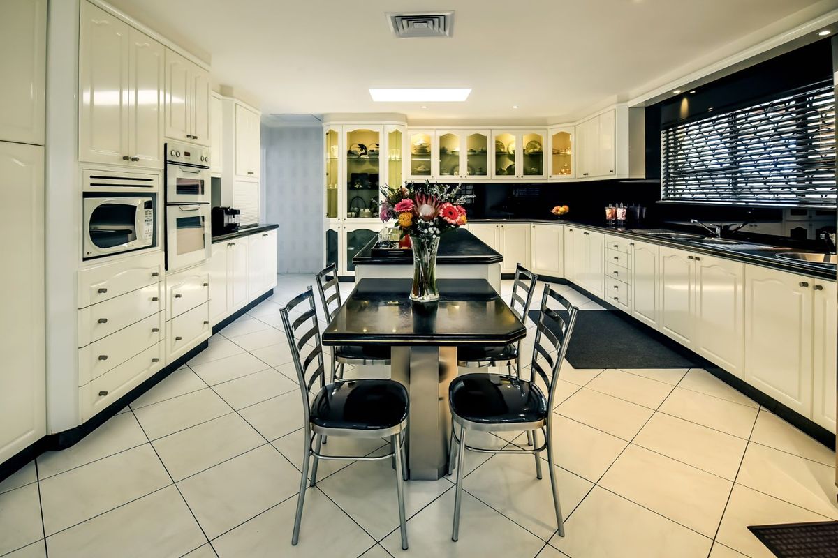 Spacious kitchen featuring high-gloss white cabinetry, integrated double ovens, built-in microwave, dark stone countertops, and a central island with integrated dining space.