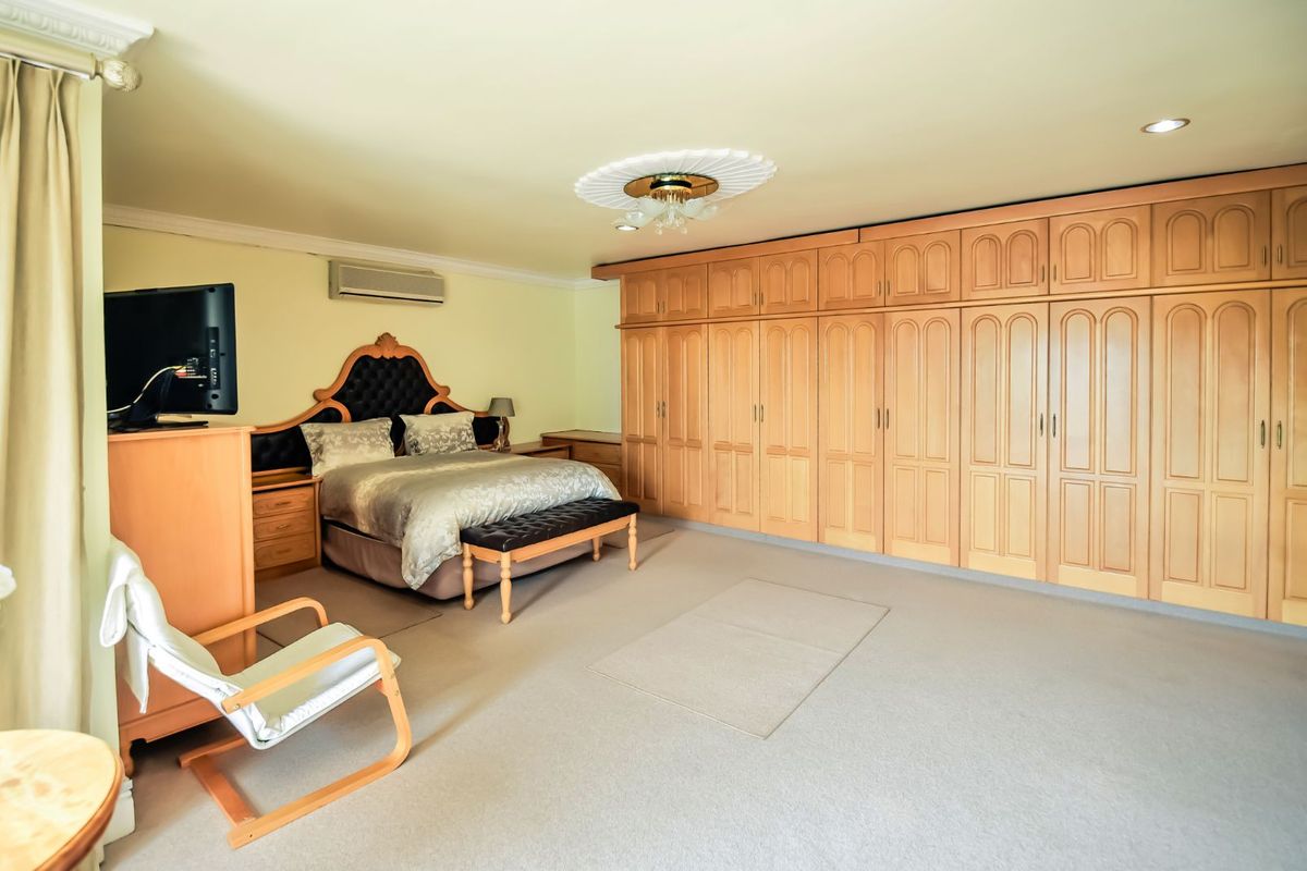 Spacious bedroom featuring extensive wall-to-wall built-in wooden cabinetry, recessed lighting, decorative ceiling rose, and a wall-mounted air conditioning unit.
