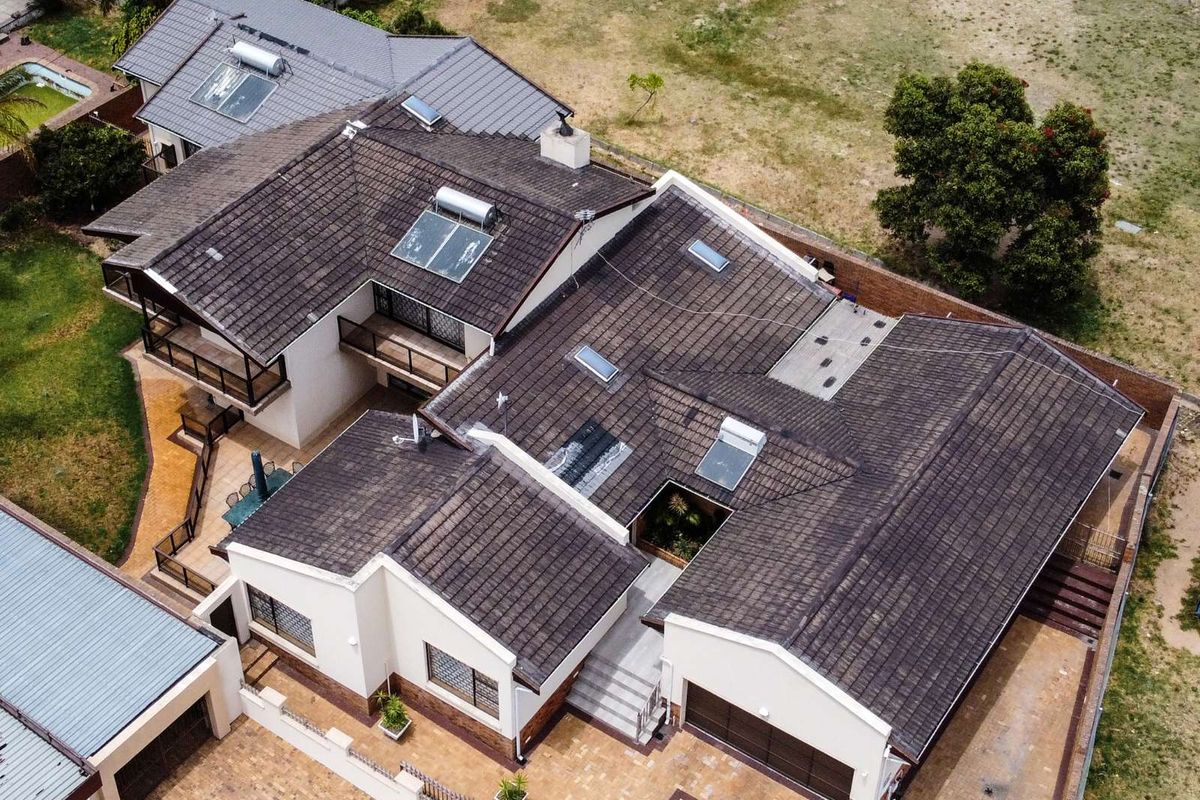 Aerial view of a large residential property featuring a multi-pitched tiled roof, solar water heating systems, skylights, and a paved driveway area.