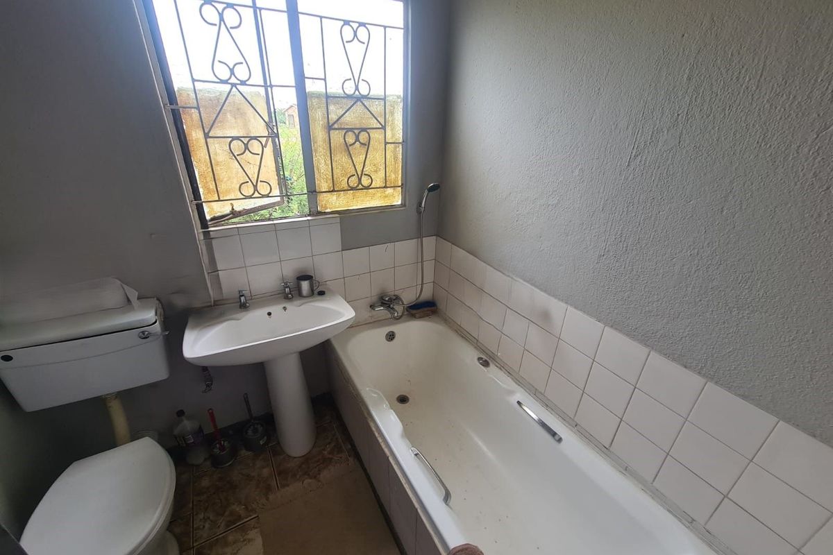 A dated bathroom featuring a standard bathtub, pedestal basin, and toilet, with security bars on the window and tiled splashbacks.