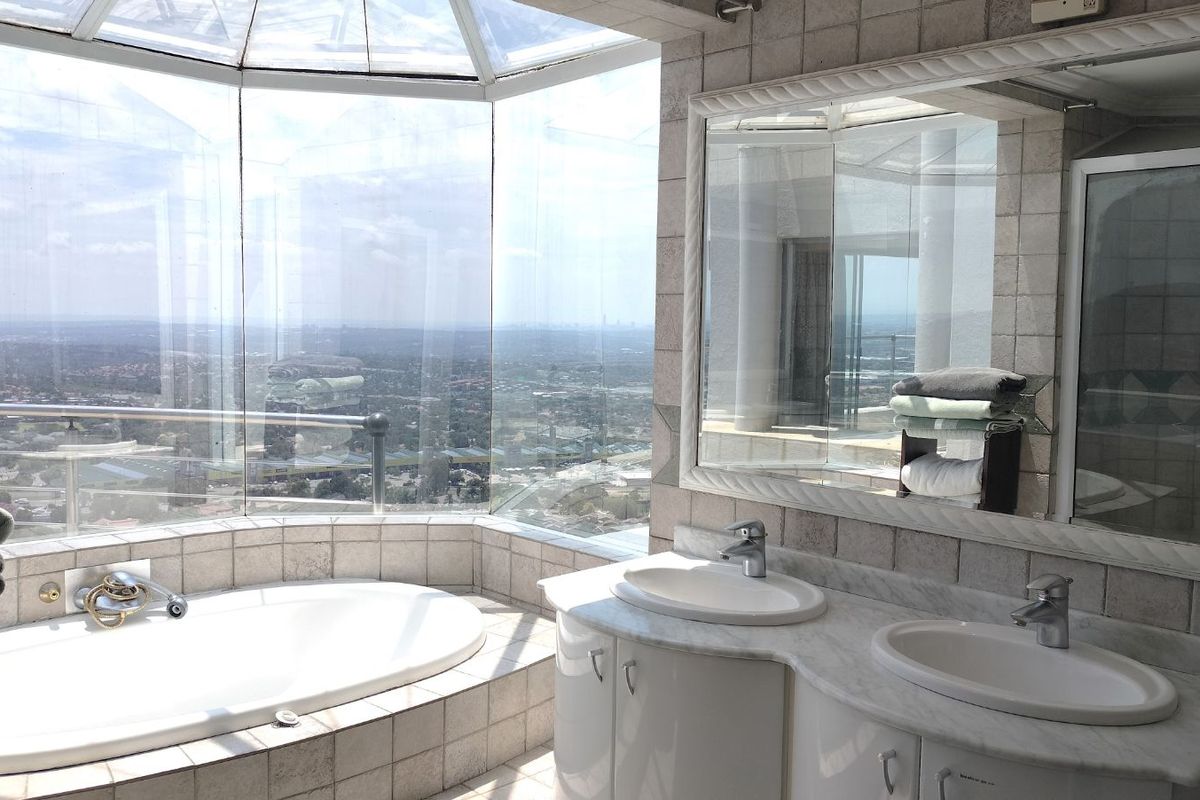 Spacious bathroom featuring a built-in oval bathtub, double vanity with marble countertop, and expansive floor-to-ceiling windows offering panoramic city views.