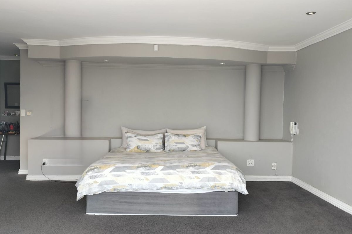 A spacious bedroom featuring a built-in headboard alcove with integrated columns, recessed downlighting, and neutral grey carpeting.