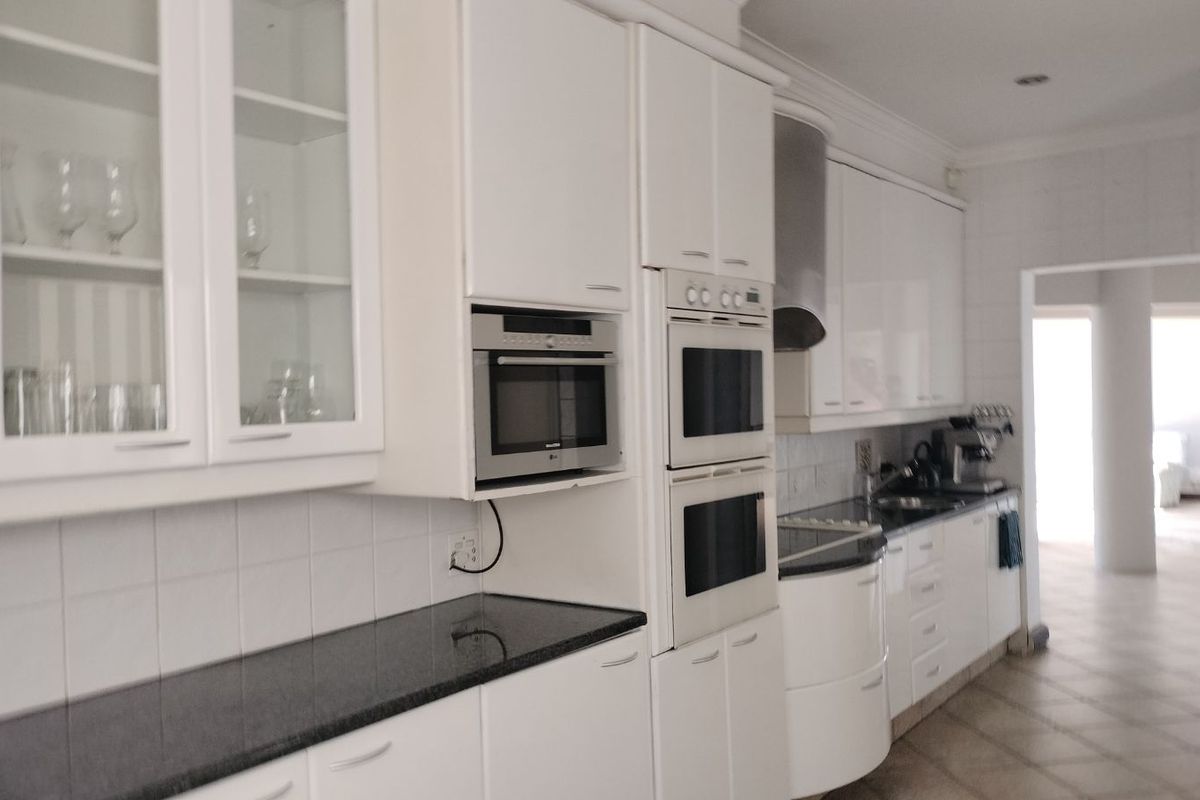 Modern kitchen featuring white cabinetry, granite countertops, built-in double ovens, microwave, and stainless steel extractor fan.