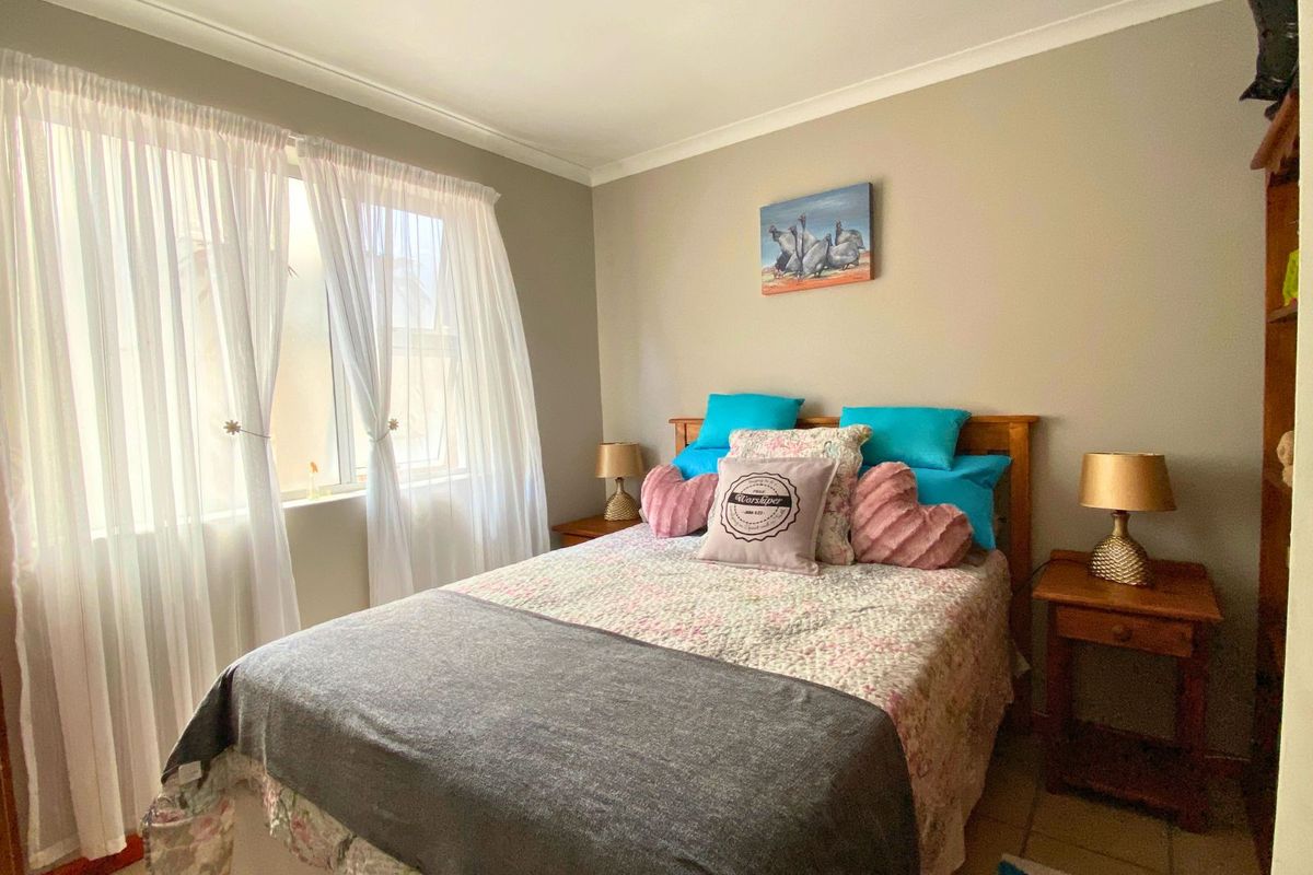 A cozy bedroom featuring tiled flooring, neutral wall tones, and a large window with sheer curtains allowing for natural light.