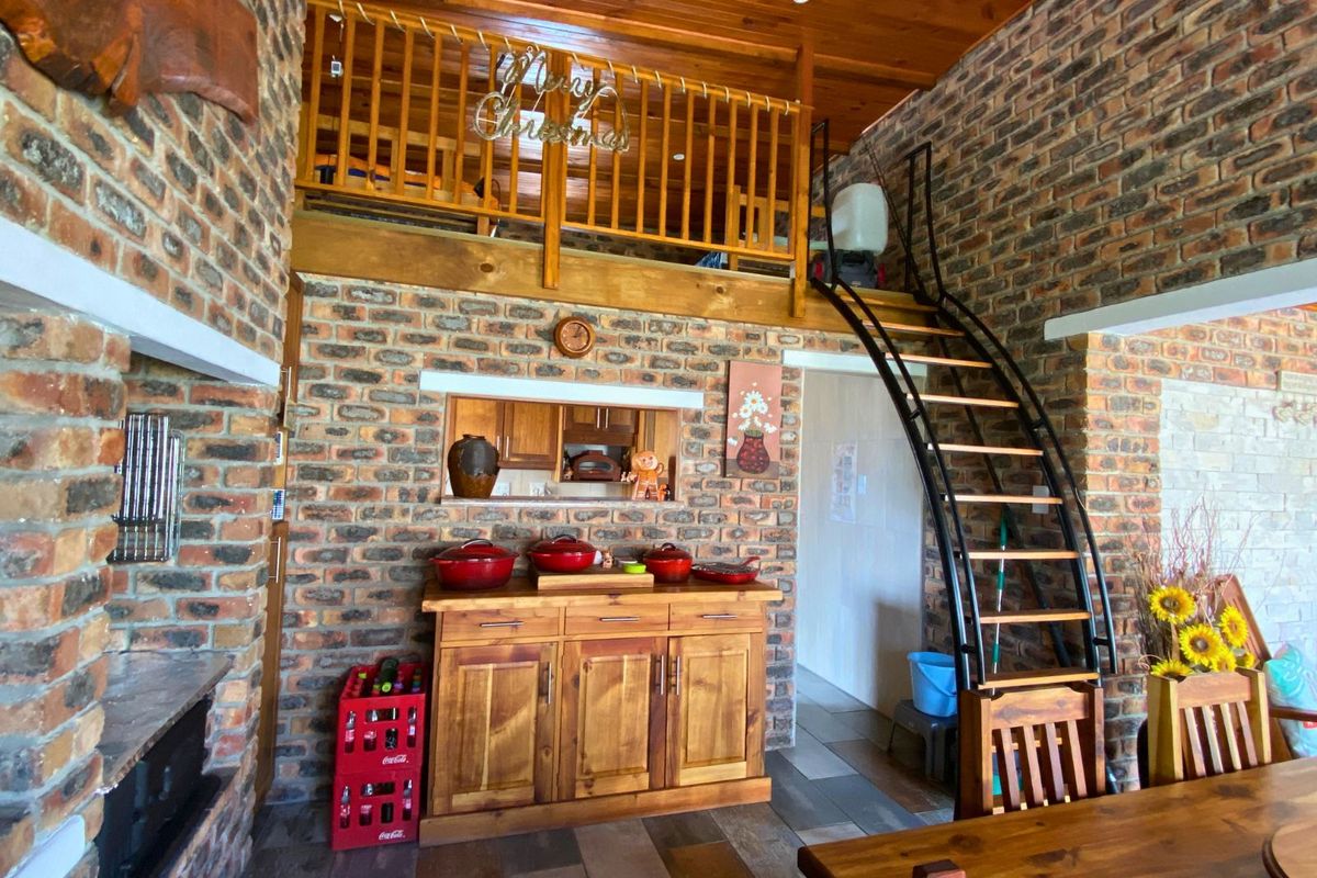 A rustic living area featuring exposed brick walls, a timber-clad ceiling, a mezzanine level with wooden balustrade, and a curved metal staircase.