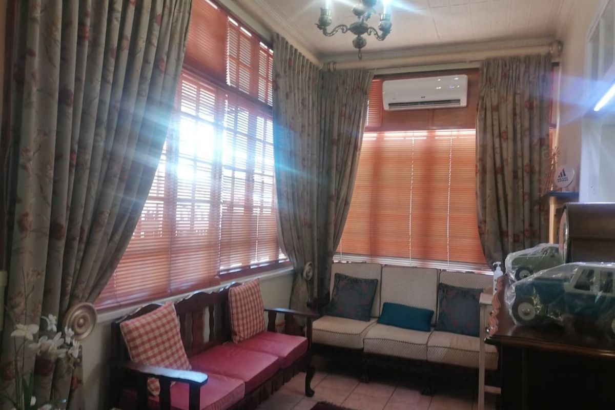 A cozy living area featuring large windows with wooden blinds, tiled flooring, and a wall-mounted air conditioning unit.