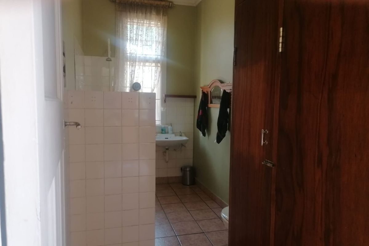 A functional bathroom featuring a tiled shower partition, wall-mounted basin, and built-in wooden cabinetry, providing a practical layout with natural light.