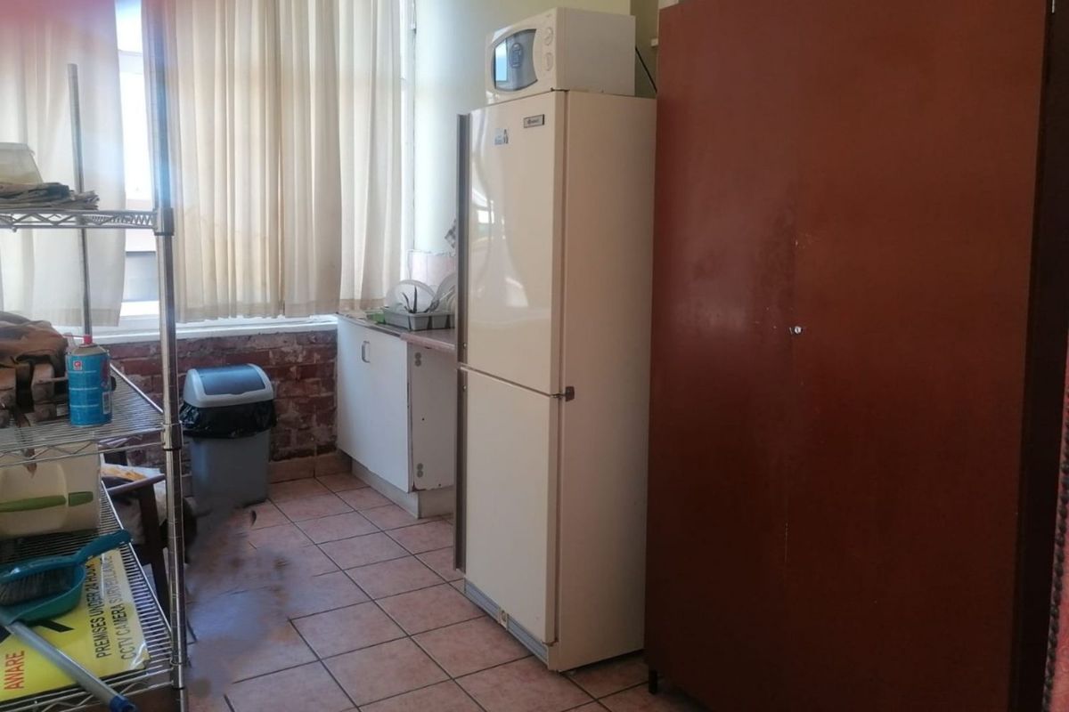 A functional kitchen area featuring tiled flooring, basic cabinetry, and a window with curtains, providing a practical workspace for staff or occupants.