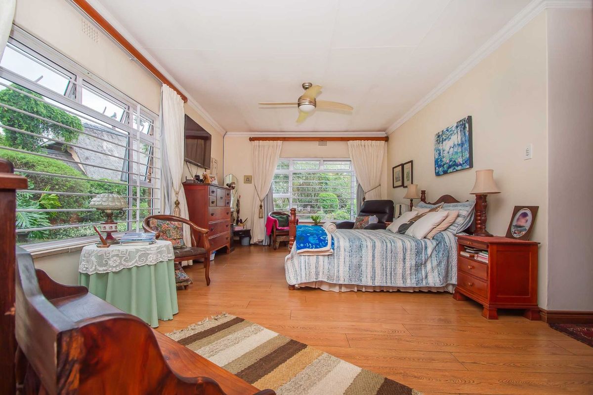 A spacious bedroom featuring large windows with security bars, wood-look flooring, and a ceiling fan.
