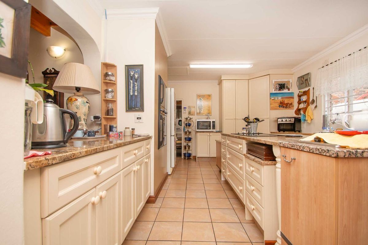 A functional kitchen featuring light-toned cabinetry, granite countertops, tiled flooring, and a central island with integrated cooktop.