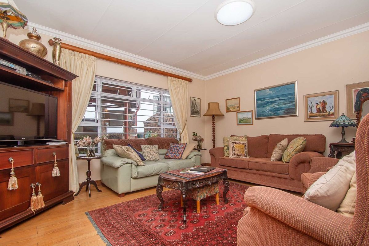 A comfortable living room featuring laminate flooring, crown molding, and large windows with security bars.
