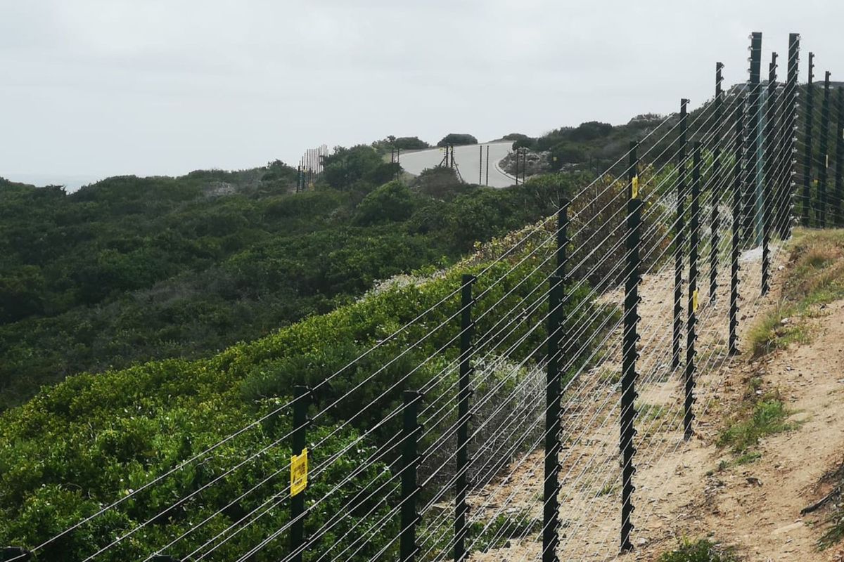 A view of the property boundary featuring a secure electric fence line along a sloped, vegetated landscape.