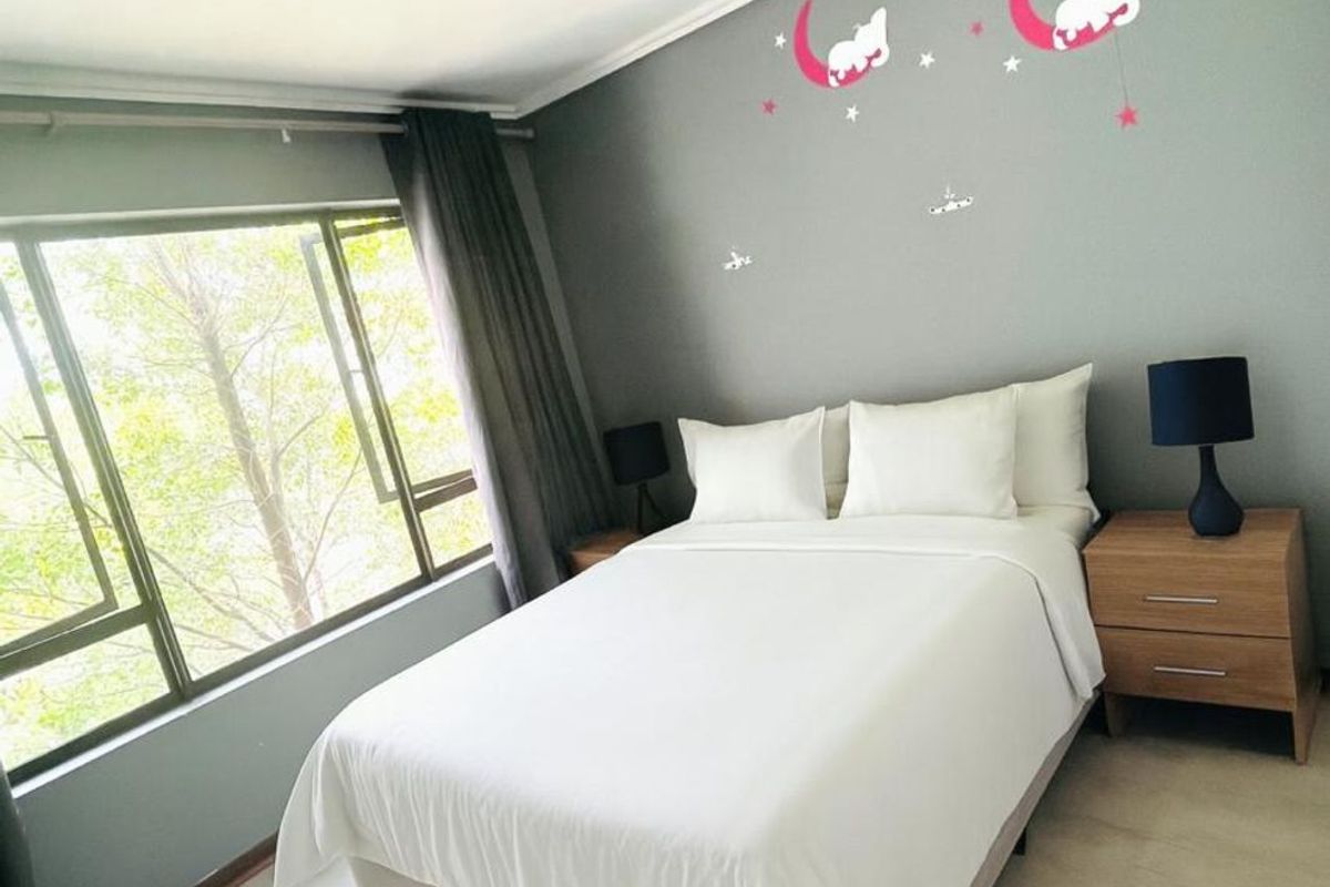 A well-lit bedroom featuring neutral grey walls, light-toned flooring, and a large window providing natural light and a pleasant outdoor view.