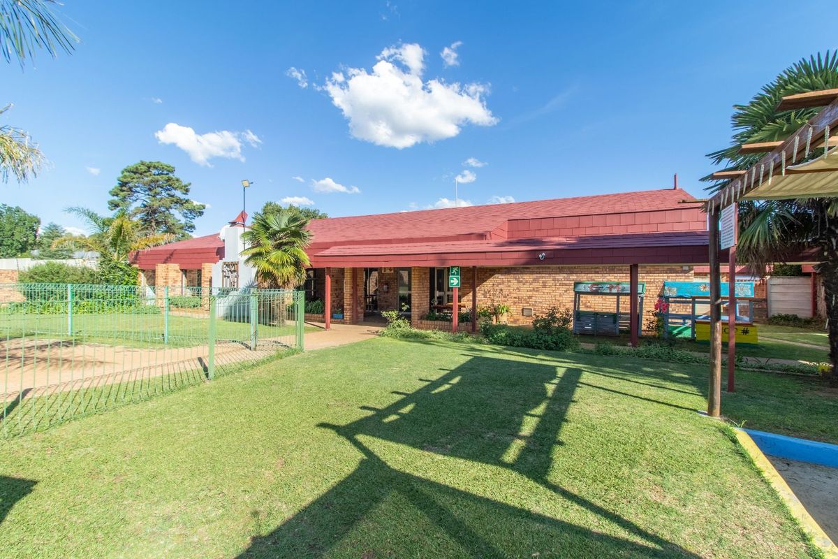 Exterior view of the guest house featuring a brick facade, covered walkway, and surrounding lawn area with perimeter fencing.