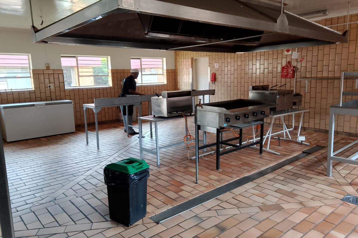 Commercial-style kitchen featuring tiled flooring, large overhead extractor hood, and stainless steel cooking stations.