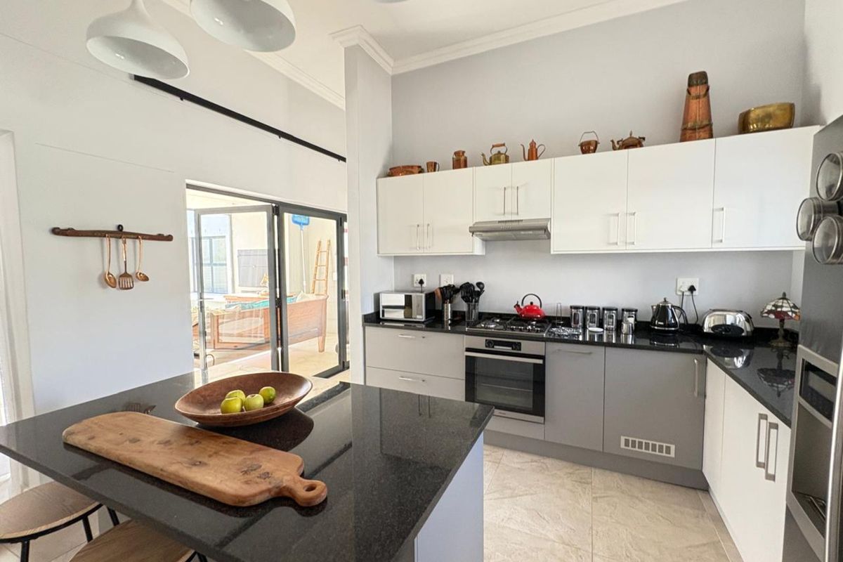 Modern kitchen featuring granite countertops, built-in oven, gas hob, extractor fan, and a central island, seamlessly flowing into the adjacent outdoor patio area.
