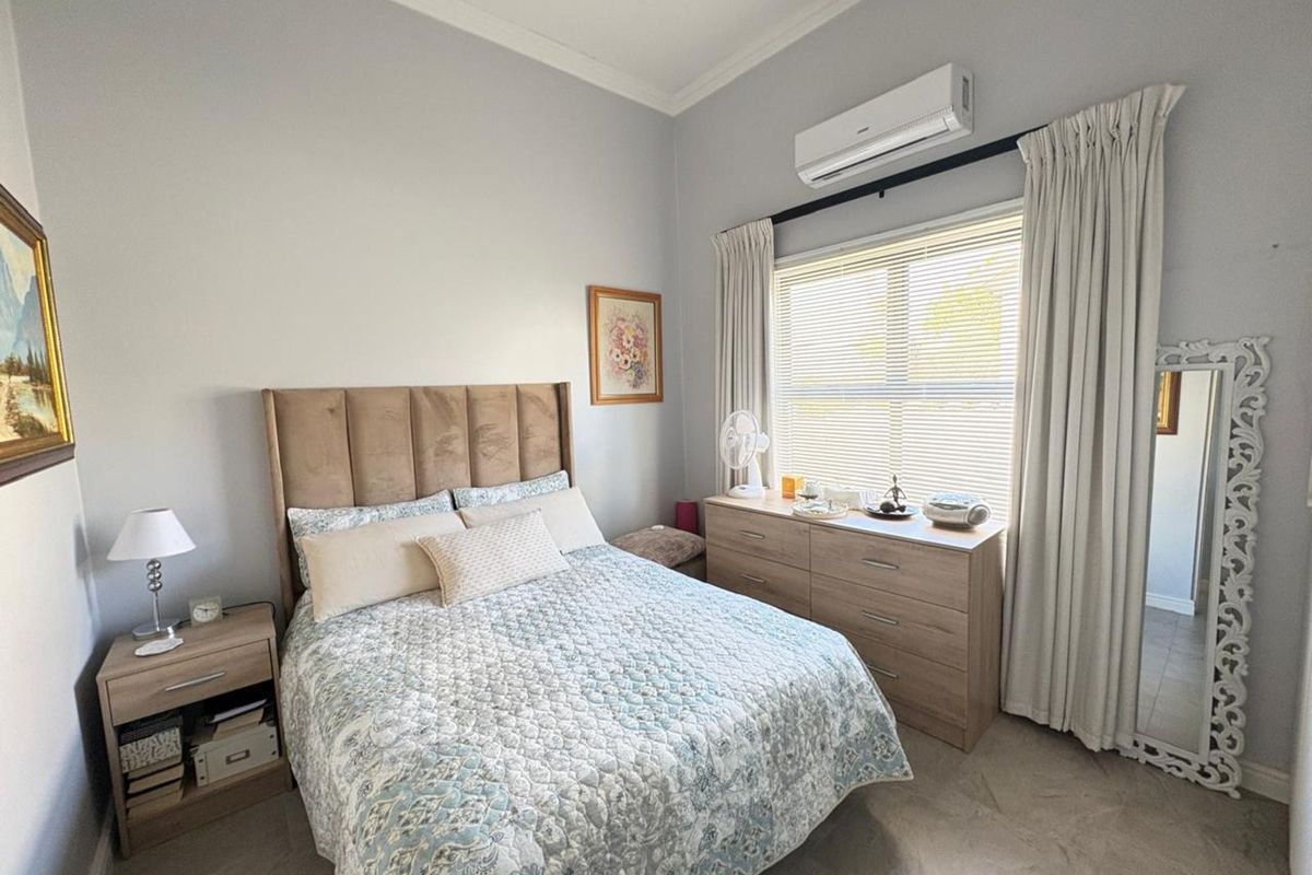 A well-maintained bedroom featuring tiled flooring, crown molding, and a wall-mounted air conditioning unit.