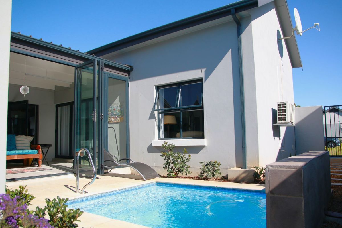 A well-maintained rear exterior view featuring a swimming pool, paved patio area, and modern folding glass doors leading into the home.