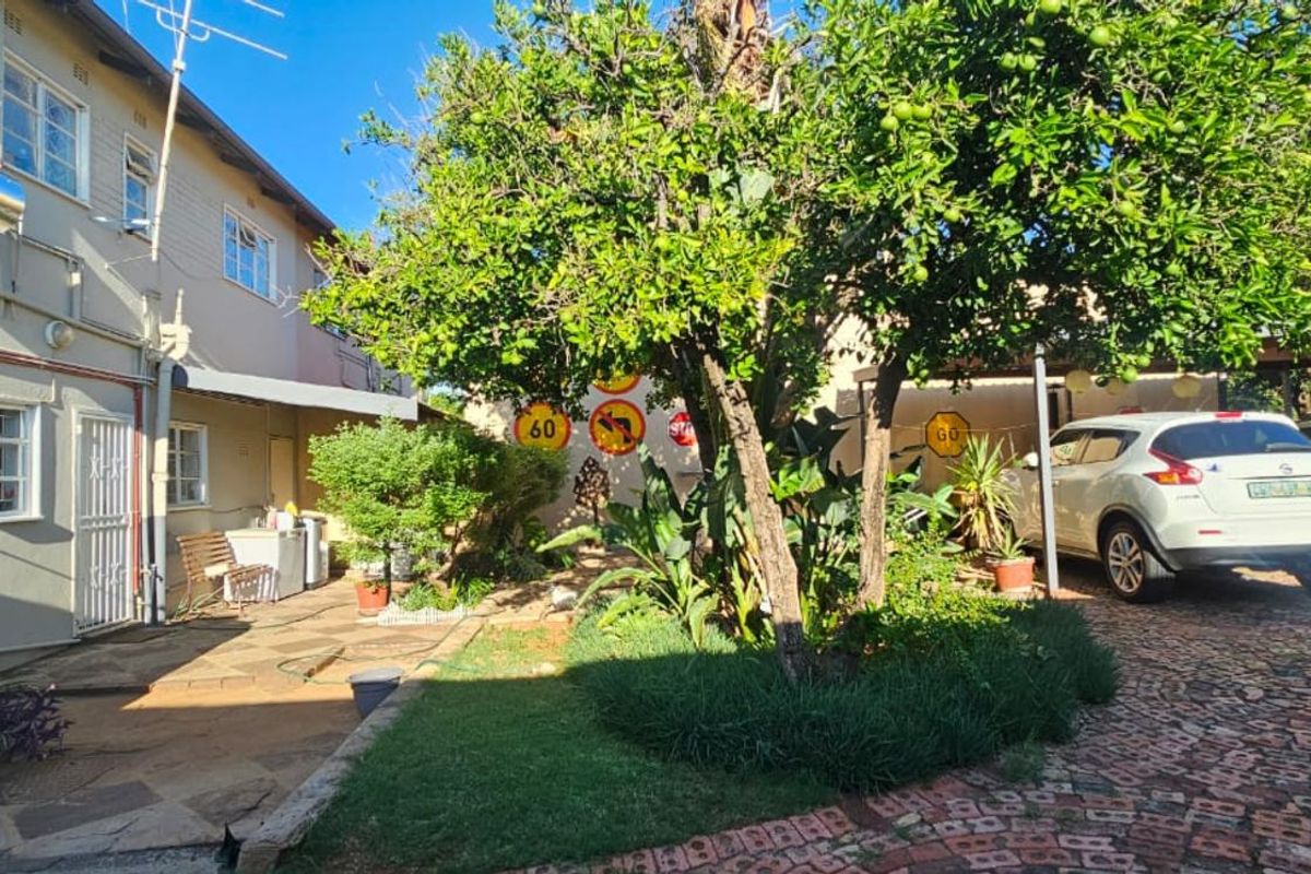 Rear exterior view featuring a paved courtyard, established garden, water storage tank, solar geyser, and covered parking area.