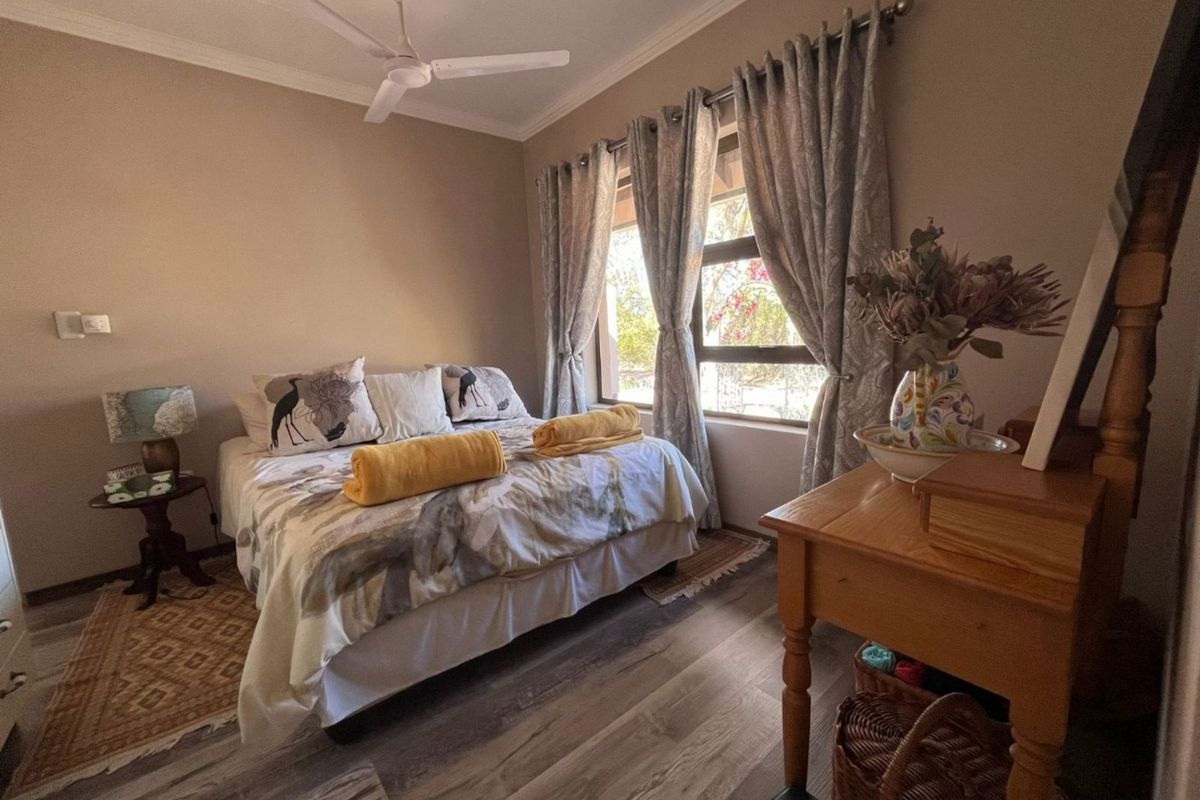 A cozy bedroom featuring wood-look flooring, a ceiling fan, and large windows that provide natural light and garden views.