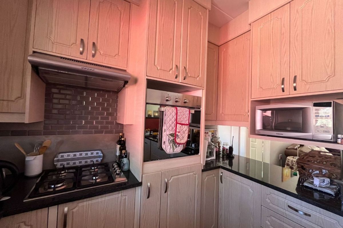 A functional kitchen featuring light wood-grain cabinetry, dark granite countertops, a built-in oven, gas hob, and a modern subway tile backsplash.
