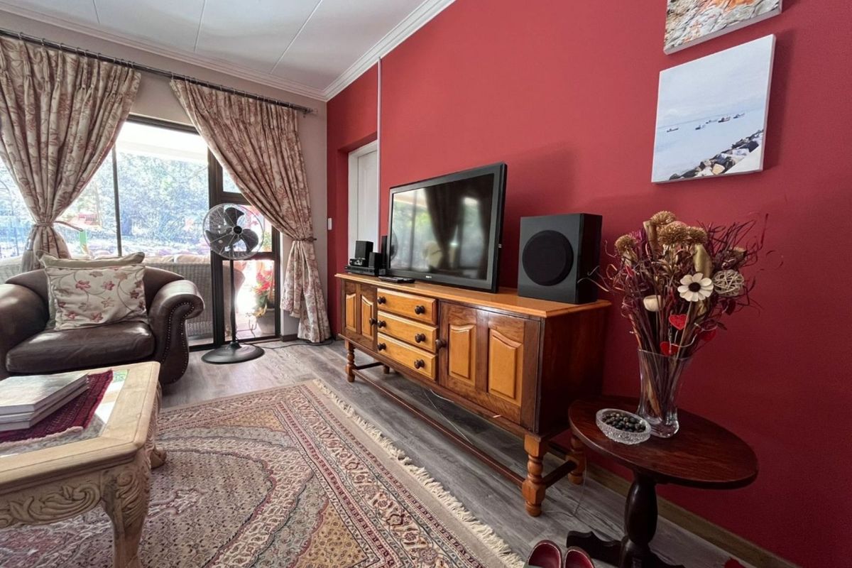 A living room featuring a bold red accent wall, wood-look flooring, and sliding glass doors providing access to an outdoor area.