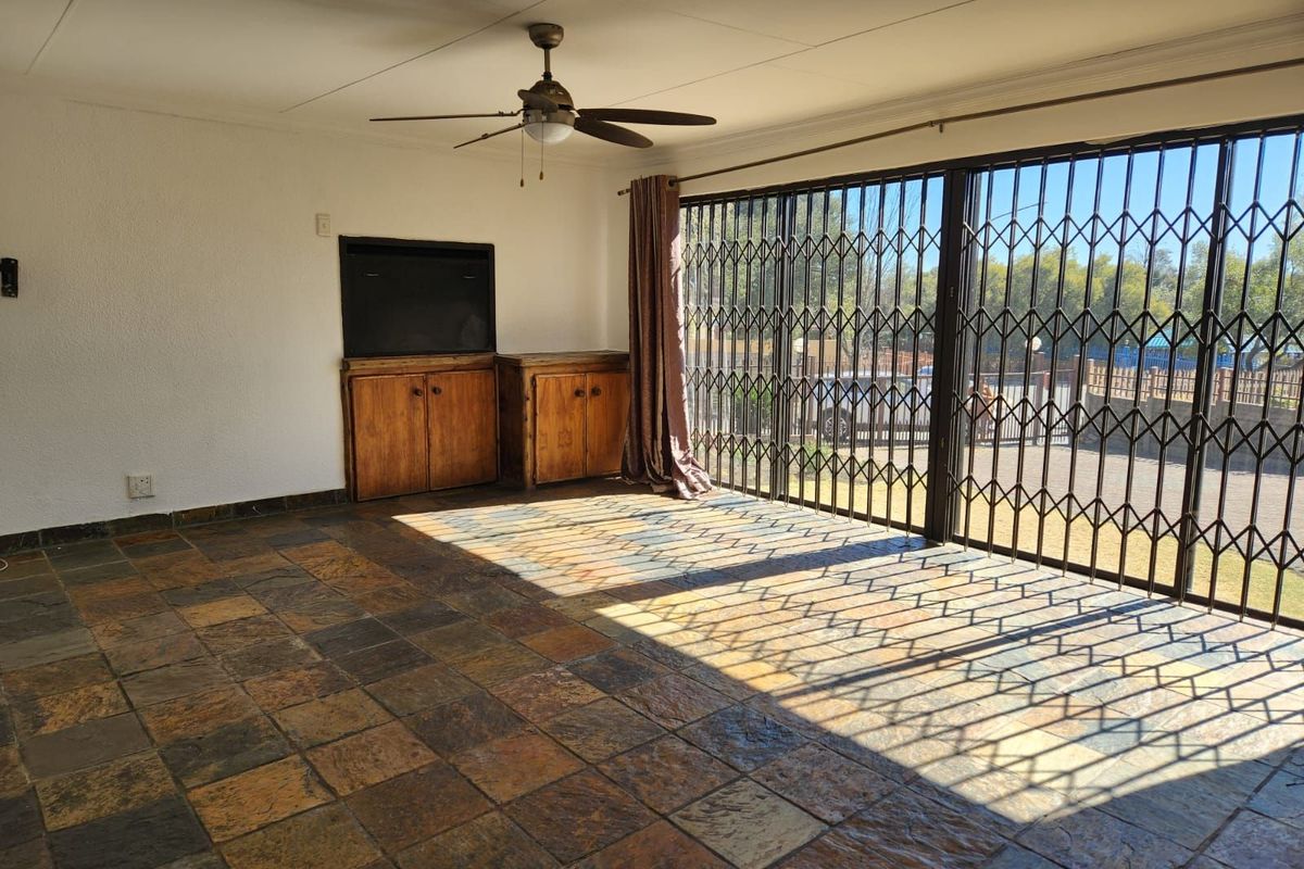 Spacious living area featuring natural stone tile flooring, a built-in wooden cabinet, ceiling fan, and large sliding glass doors with security gates.