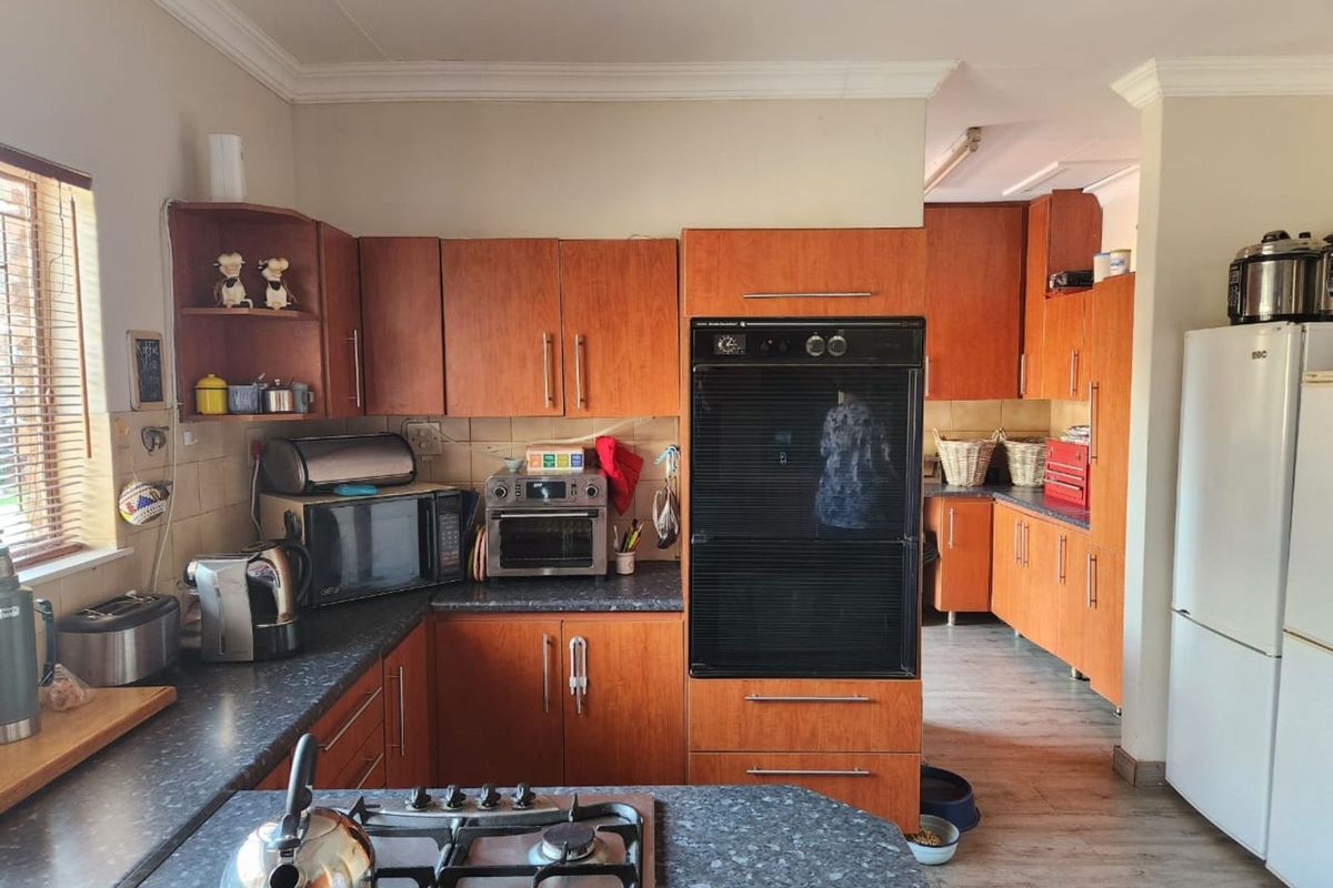 A functional kitchen featuring wood-veneer cabinetry, dark laminate countertops, a built-in double oven, and a gas hob, with an adjacent scullery area.