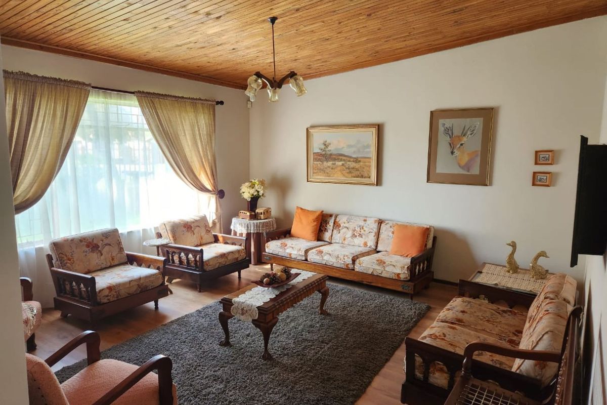 A traditional living room featuring a warm timber-clad ceiling, laminate flooring, and large windows that provide ample natural light.
