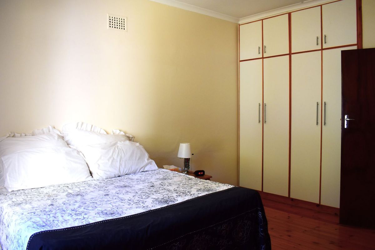 A bedroom featuring built-in floor-to-ceiling wardrobes with timber trim and polished timber flooring.