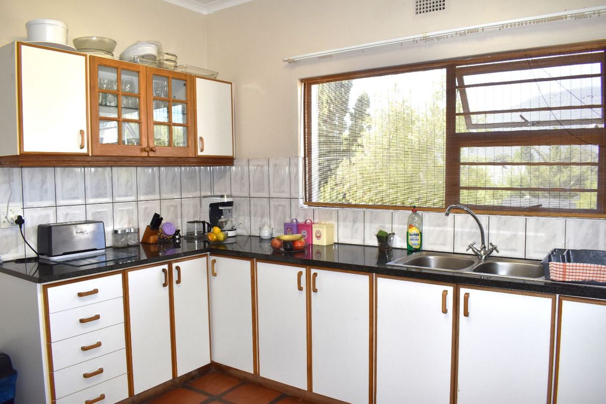 A functional kitchen featuring white cabinetry with wood trim, dark granite countertops, tiled backsplash, and a double stainless steel sink under a large window.