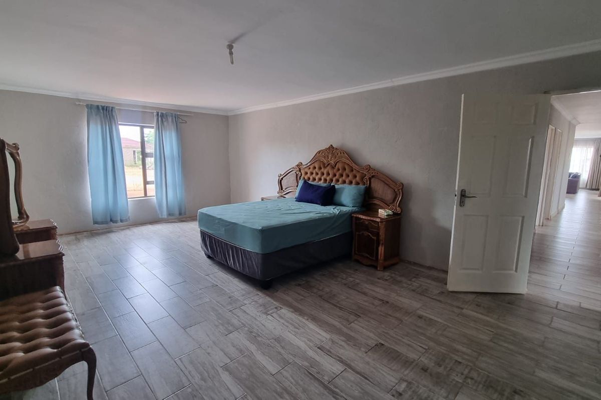 Spacious bedroom featuring wood-look tiled flooring, neutral wall finishes, and a window providing natural light, with direct access to the hallway.