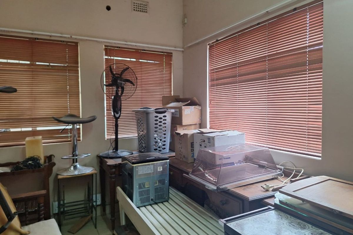 A corner room featuring multiple windows with wooden blinds, tiled flooring, and visible wall ventilation points.