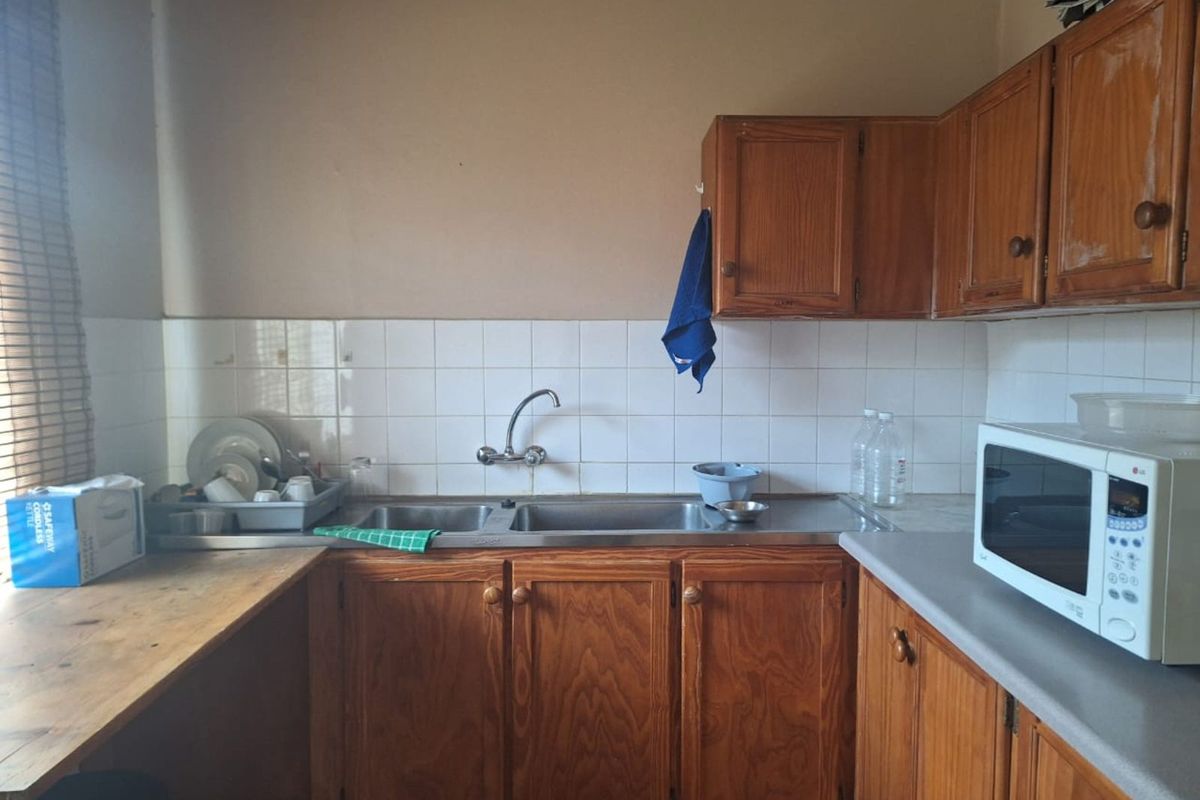 A dated kitchen area featuring wooden cabinetry, a double stainless steel sink, and a tiled backsplash.