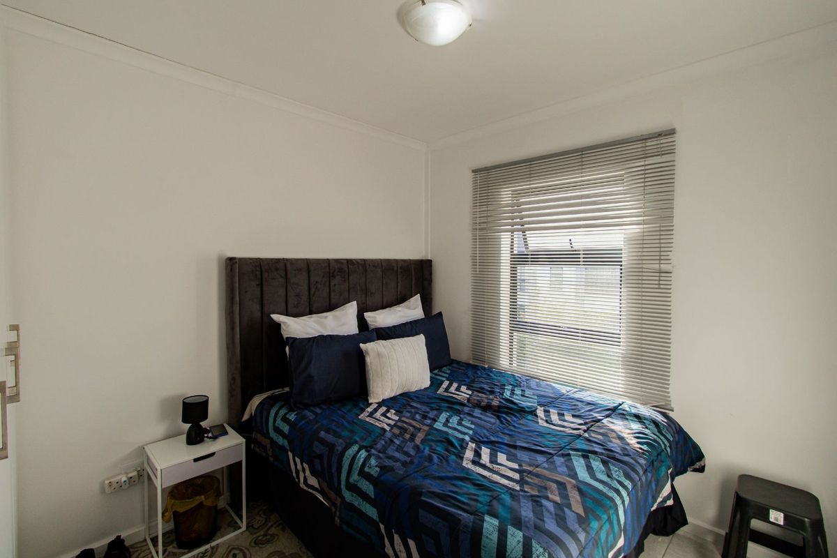 A compact bedroom featuring a window with fitted horizontal blinds and a central ceiling light fixture.