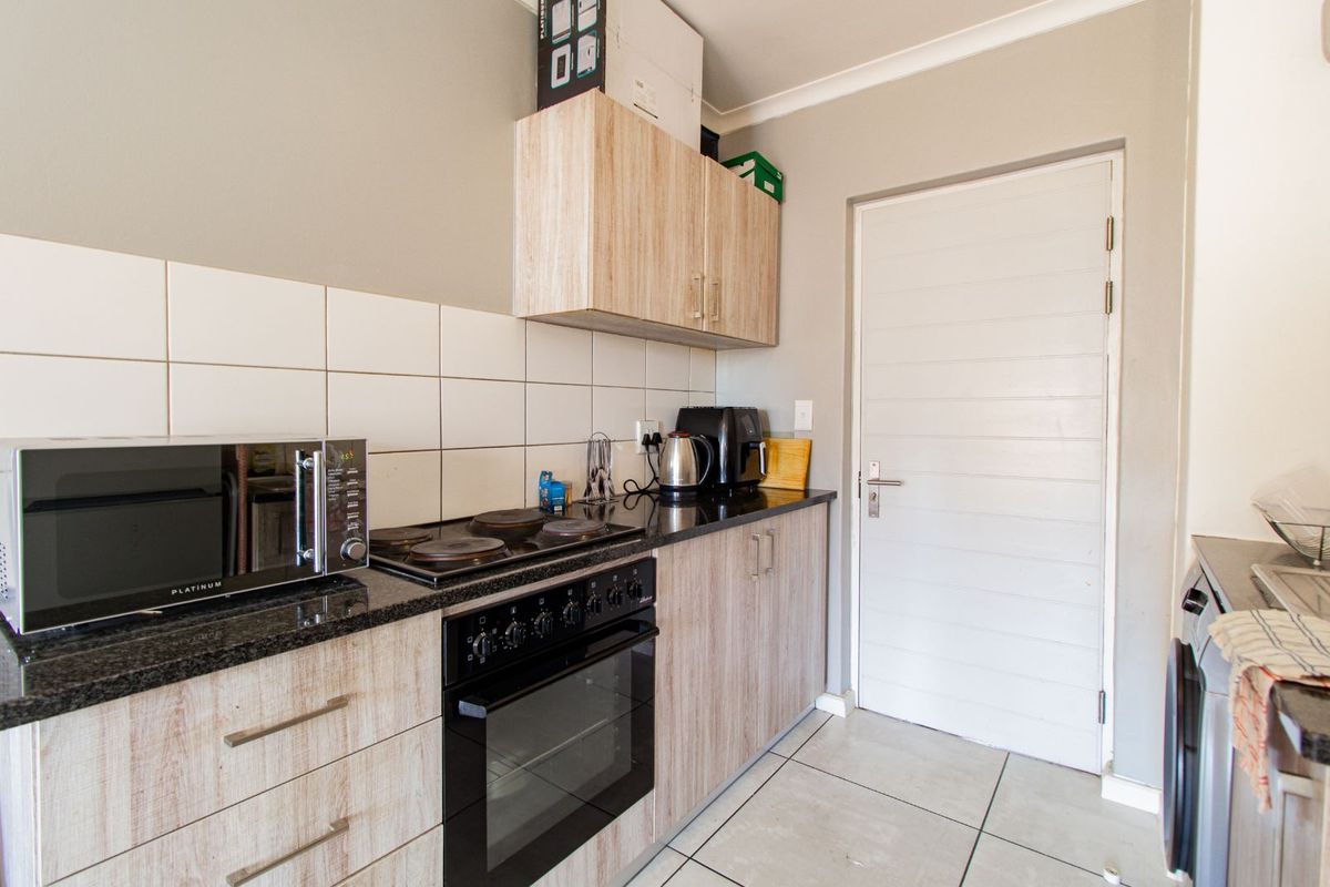 Compact kitchen featuring light wood-grain cabinetry, black granite countertops, a built-in oven with hob, and tiled splashbacks.