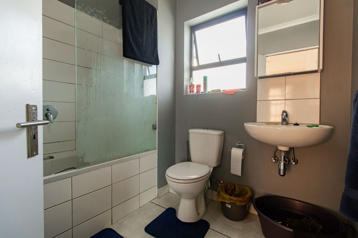 A functional bathroom featuring a shower-over-bath combination, wall-mounted basin, and toilet with tiled flooring and neutral wall finishes.