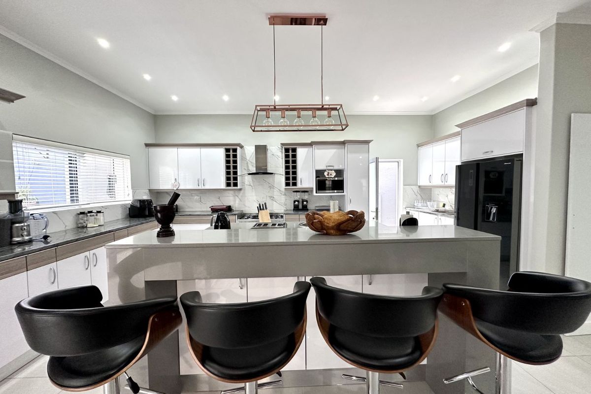 Modern kitchen featuring a central island with breakfast bar, sleek cabinetry, stone countertops, built-in oven, extractor fan, and contemporary pendant lighting.