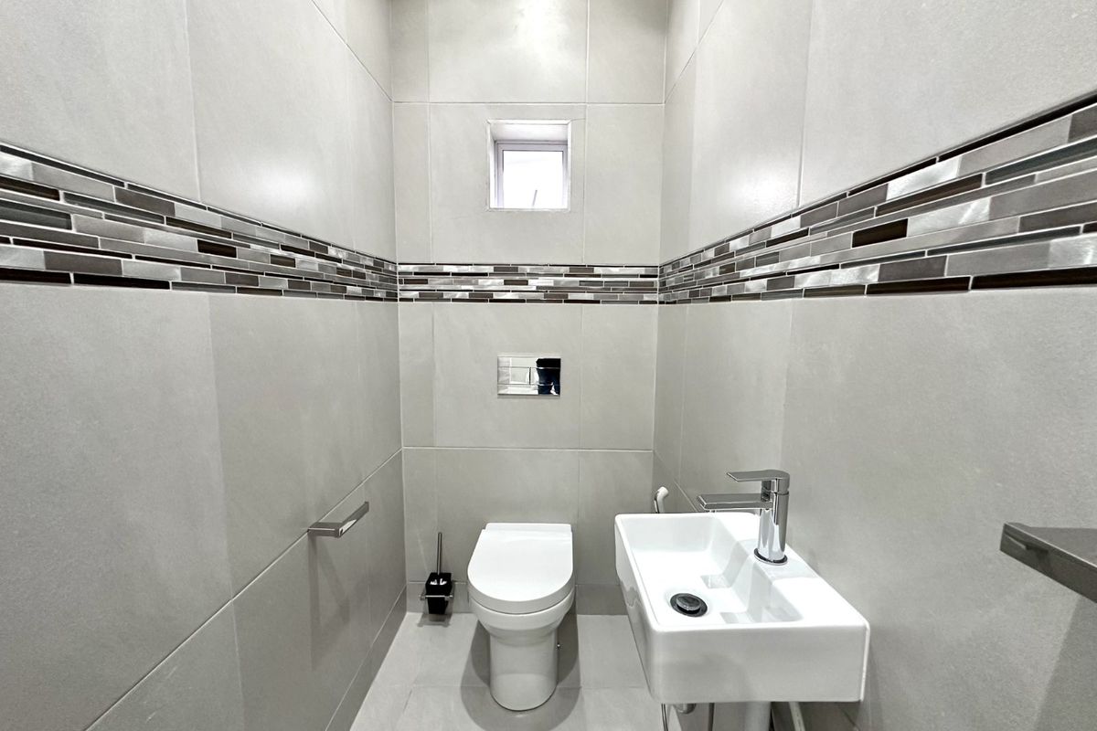 A modern, compact guest bathroom featuring floor-to-ceiling neutral tiling, a wall-mounted toilet with a concealed cistern, and a sleek wall-hung basin.
