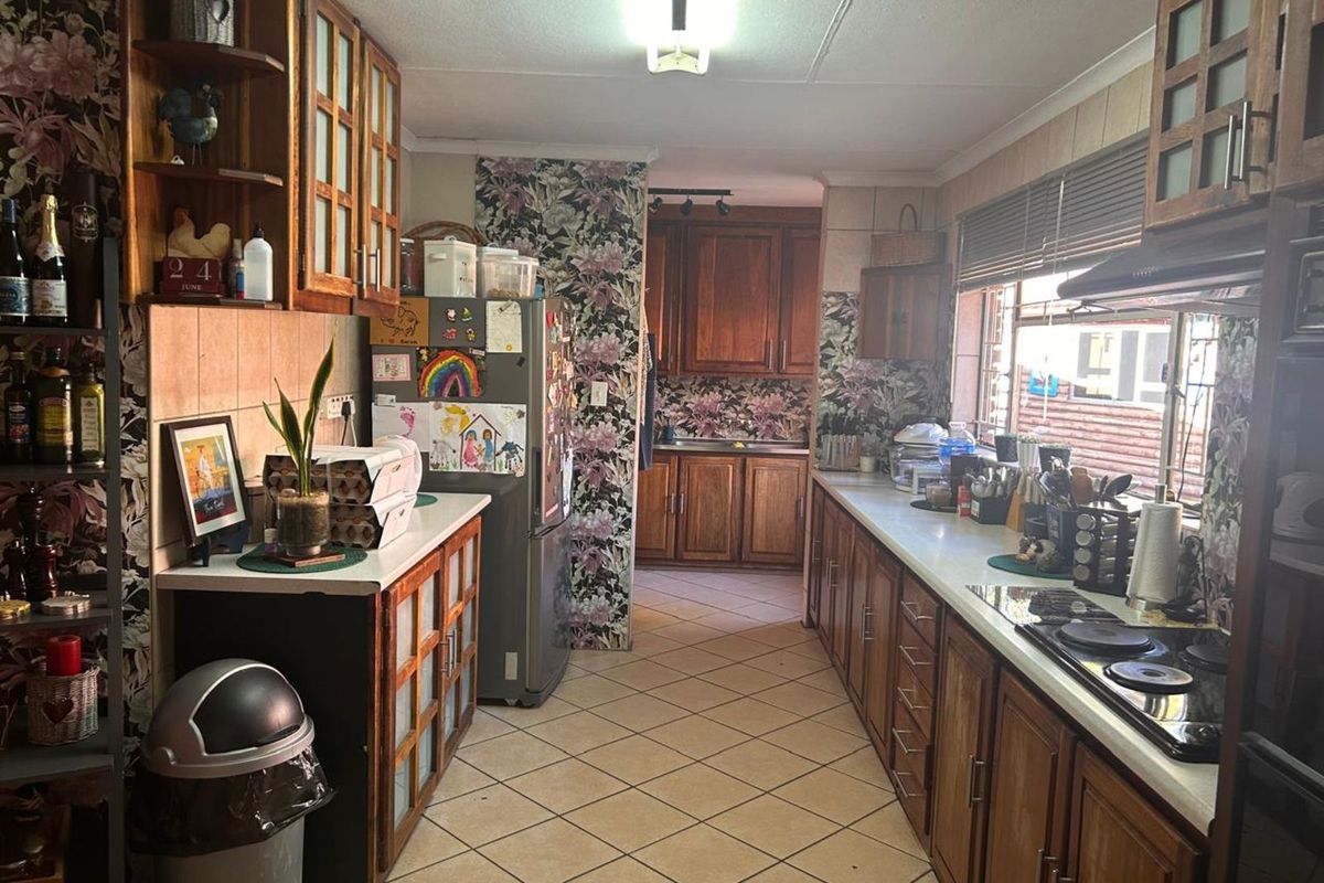 A functional galley-style kitchen featuring timber cabinetry, tiled flooring, and integrated cooktop, offering ample storage and counter space.