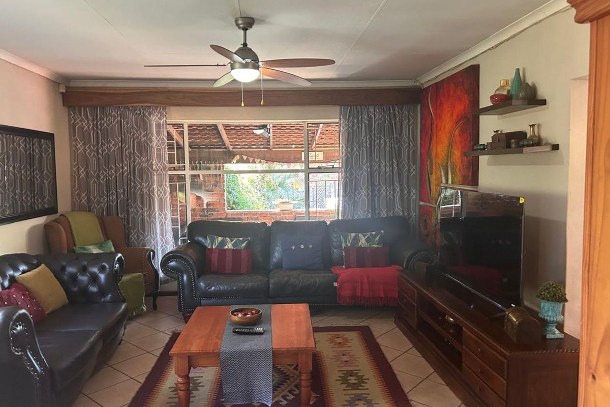 A comfortable living room featuring tiled flooring, a ceiling fan, and large windows providing natural light and a view of the outdoor patio area.