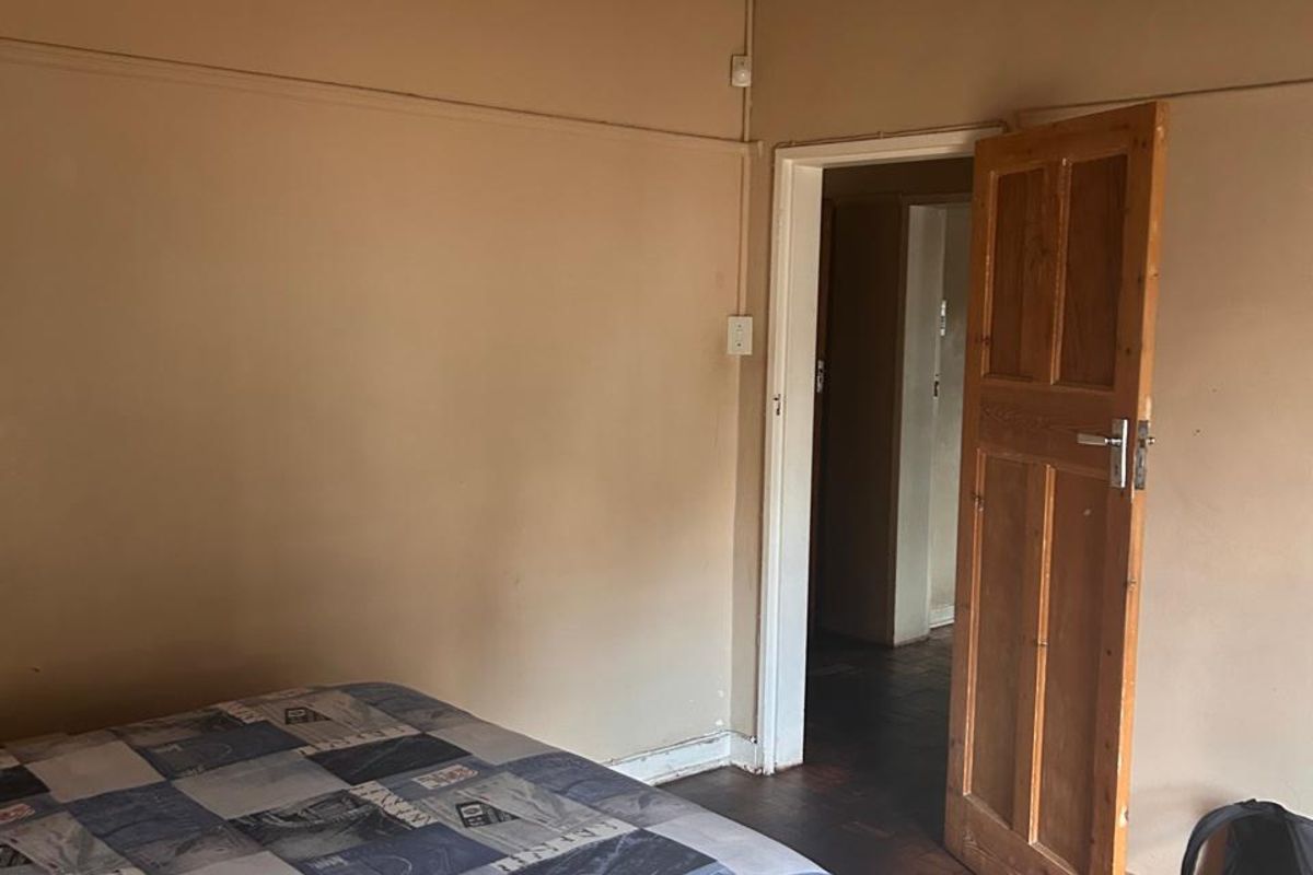 A bedroom featuring original parquet flooring and a wooden door, currently requiring ceiling repairs and cosmetic updates to the wall finishes.