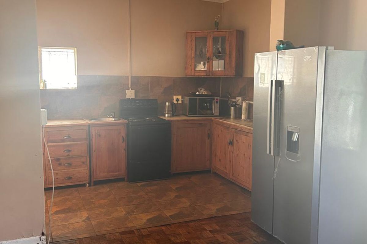 A dated kitchen featuring wooden cabinetry, tiled splashbacks, and parquet flooring, offering a functional layout with potential for modern renovation.