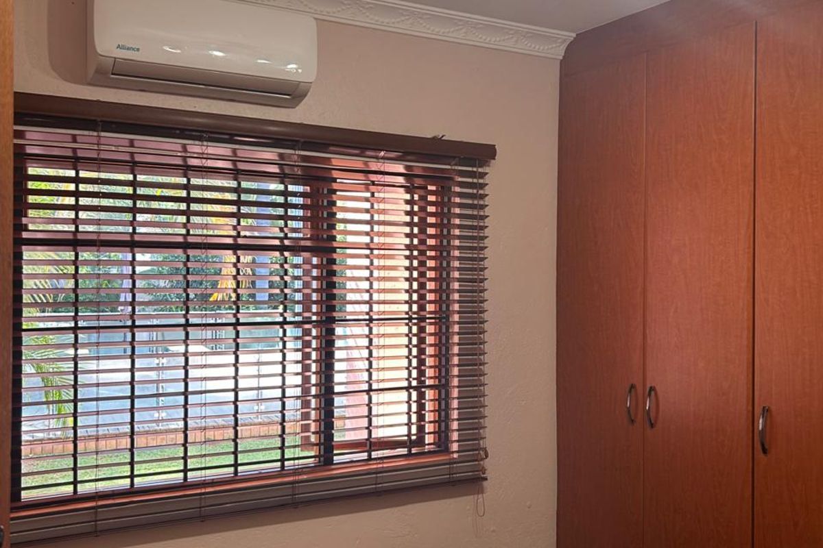 A bedroom featuring built-in wooden cupboards, a wall-mounted air conditioning unit, and a multi-directional ceiling light fixture.